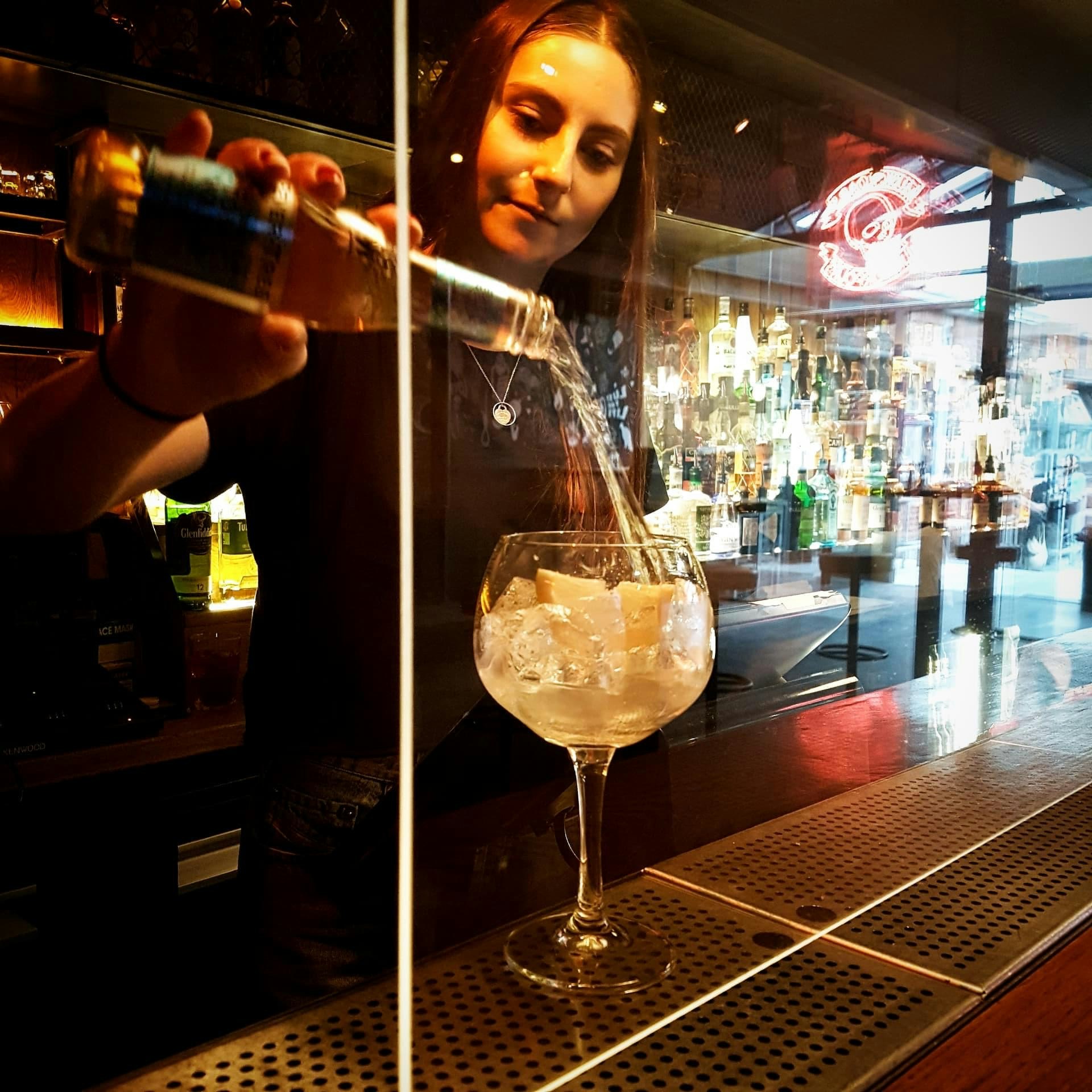 A bartender prepares a drink behind a transparent screen