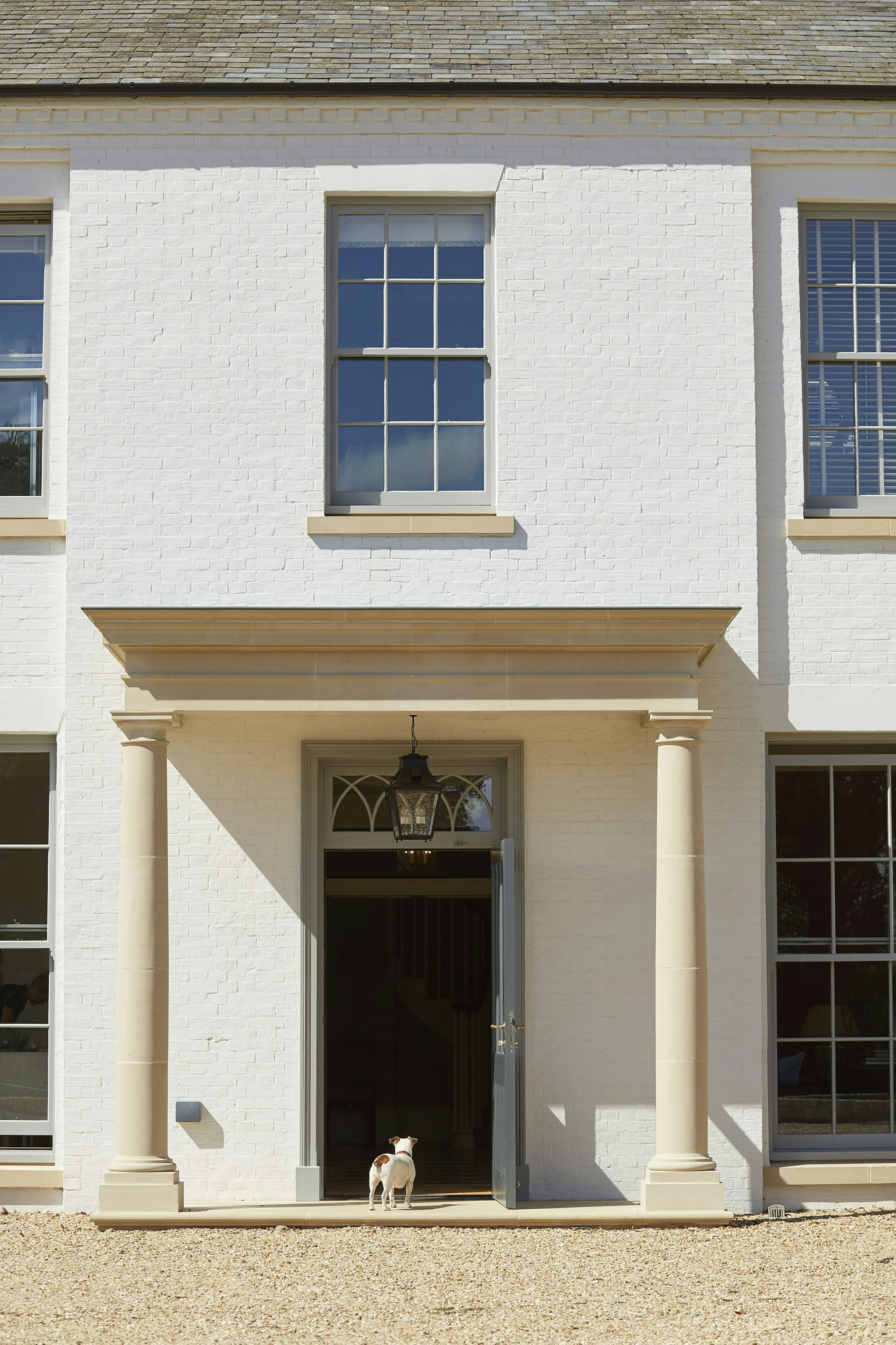 A large white building with a small terrier dog standing in the doorway facing in to the hotel