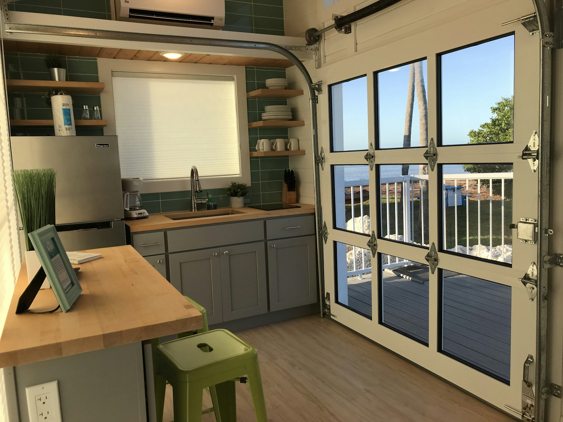 A smart interior of a tiny house, with a fully equipped kitchen and doors that open up on to a decked area.