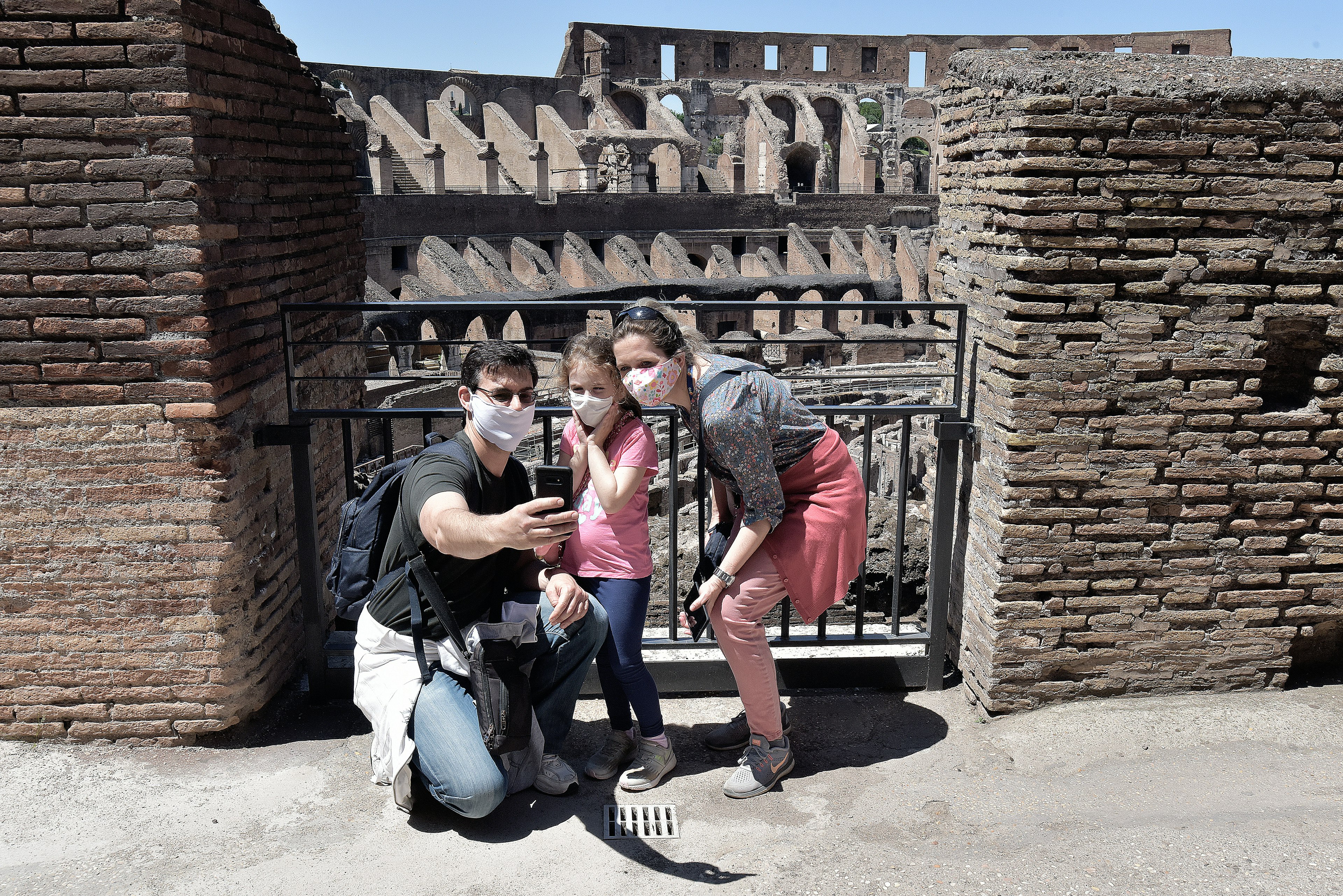 The Colosseum reopens to the public. A family of three, all wearing masks, pose for a selfie within the ancient monument