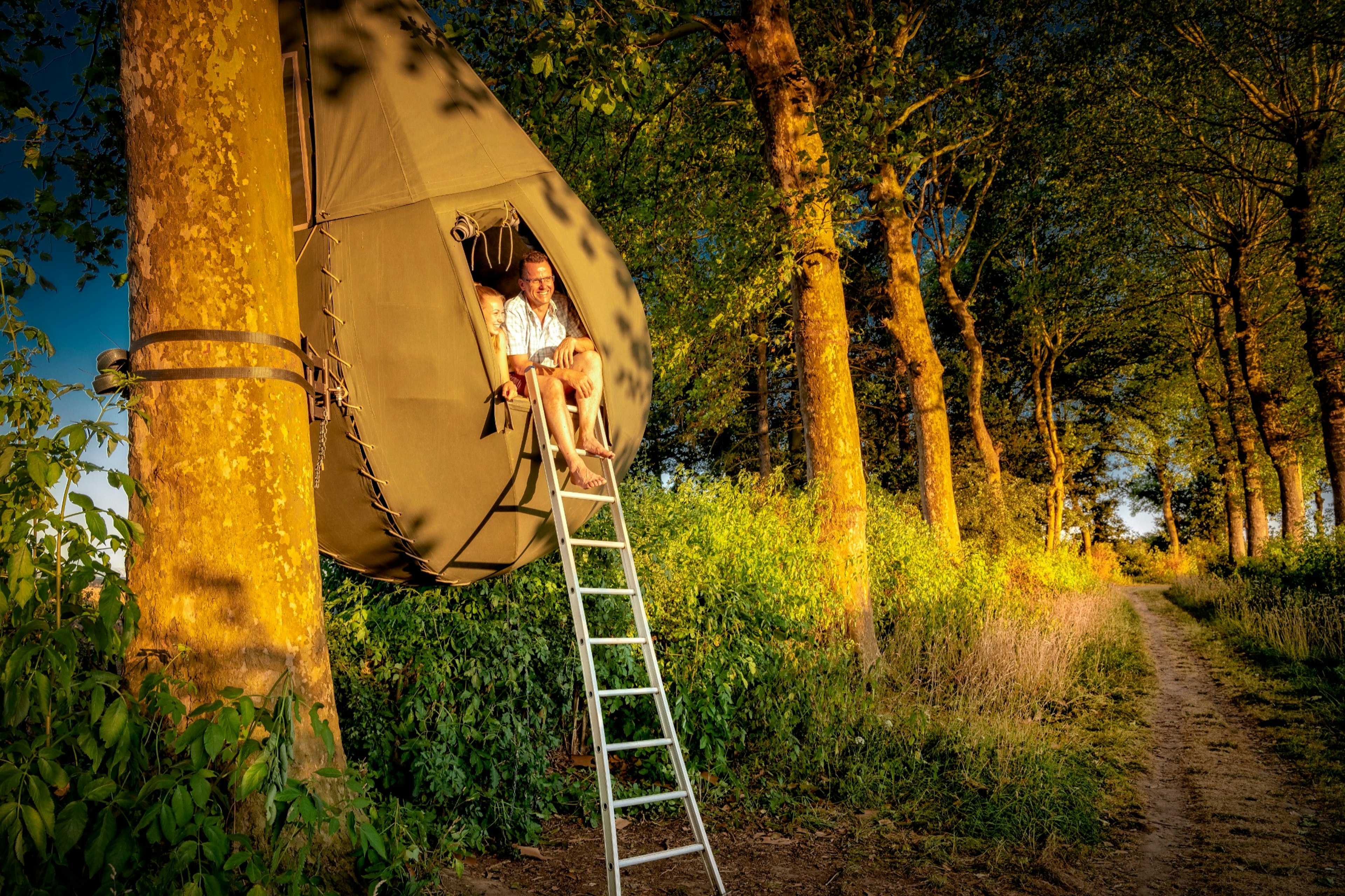 People sittng at the entrance of the teardrop-shaped tents suspended from trees in Belgium