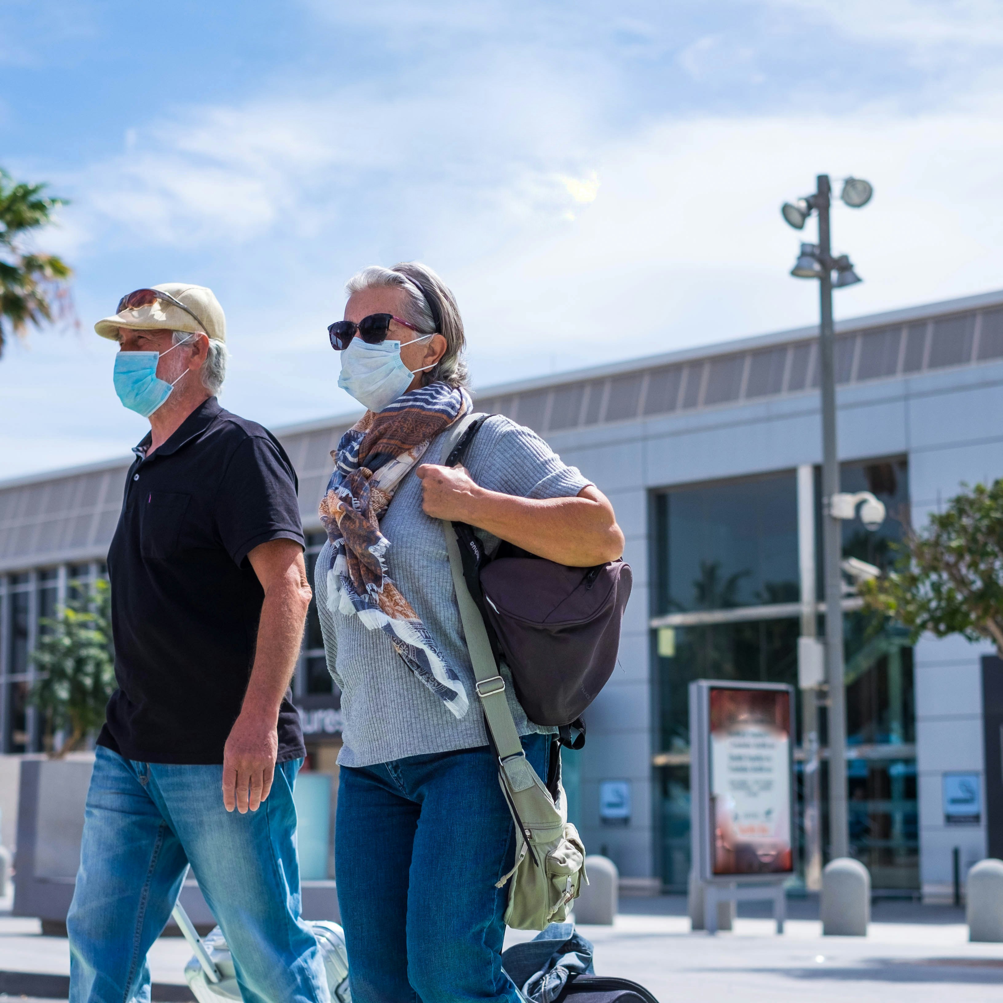 two senior walking with their baggage and wearing medical mask to prevent covid-19 or coronavirus or another type of virus or disease - safe travelers concept and lifestyle walking outdoor
