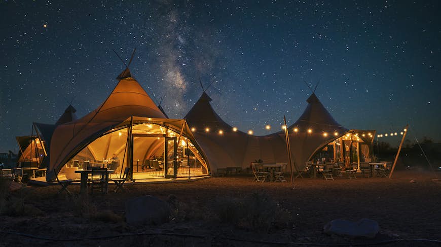 A safari-style tent with a large white canopy and string lights hanging outside. It's night and the stars are brightly shining down, filling the sky