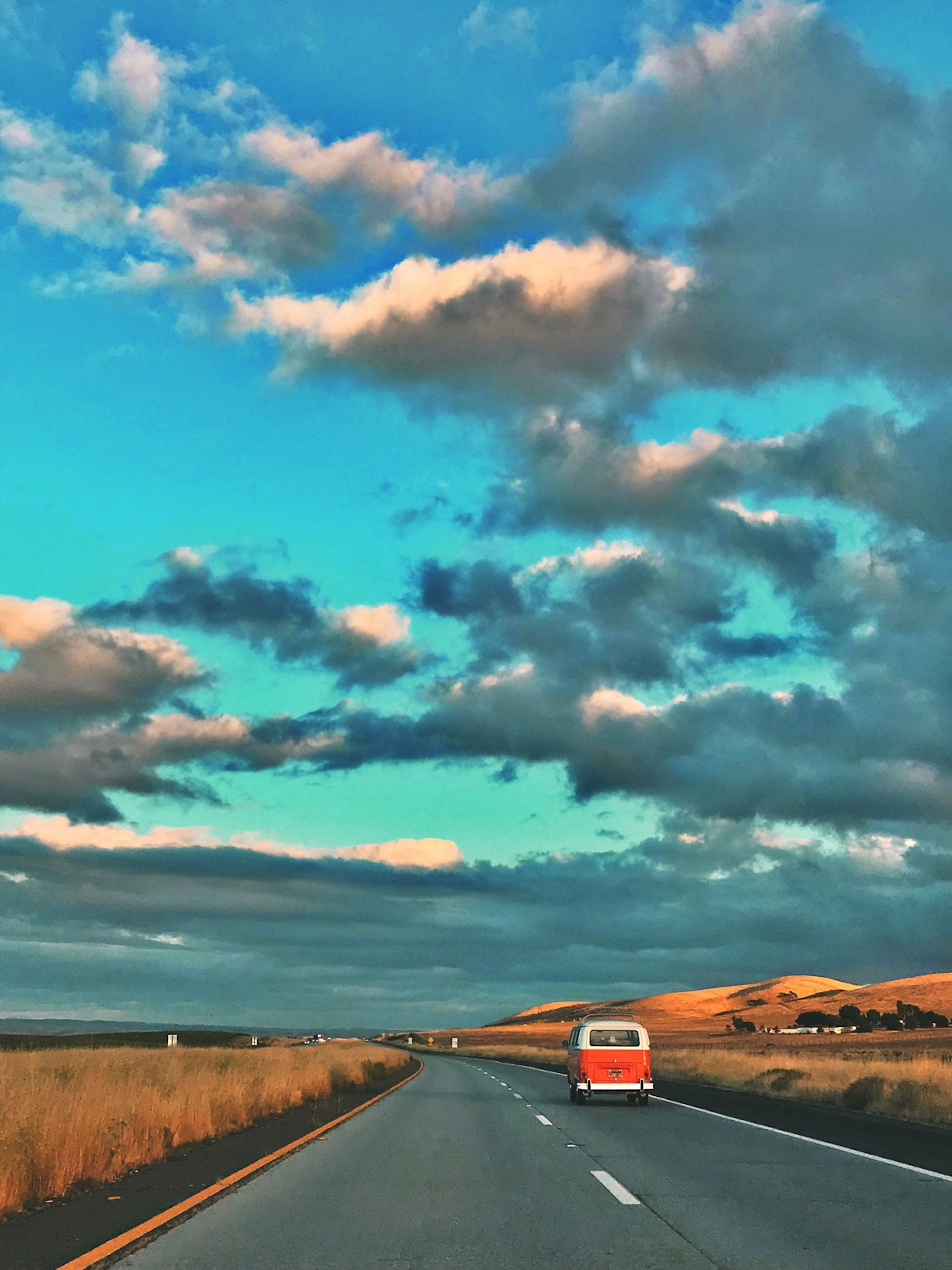 An orange VW camper cruises down a two-lane highway