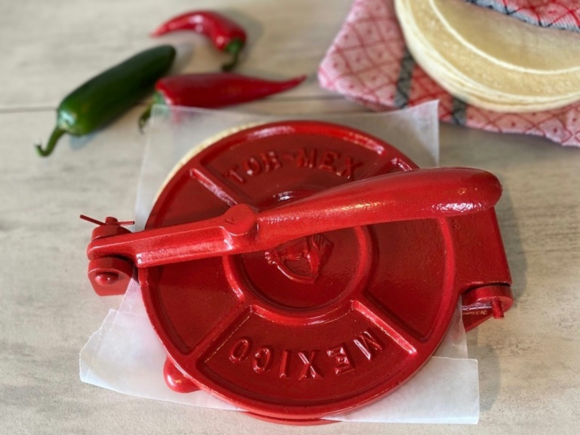 Verve Culture's red tortilla press with chili peppers and a folded napkin holding tortillas