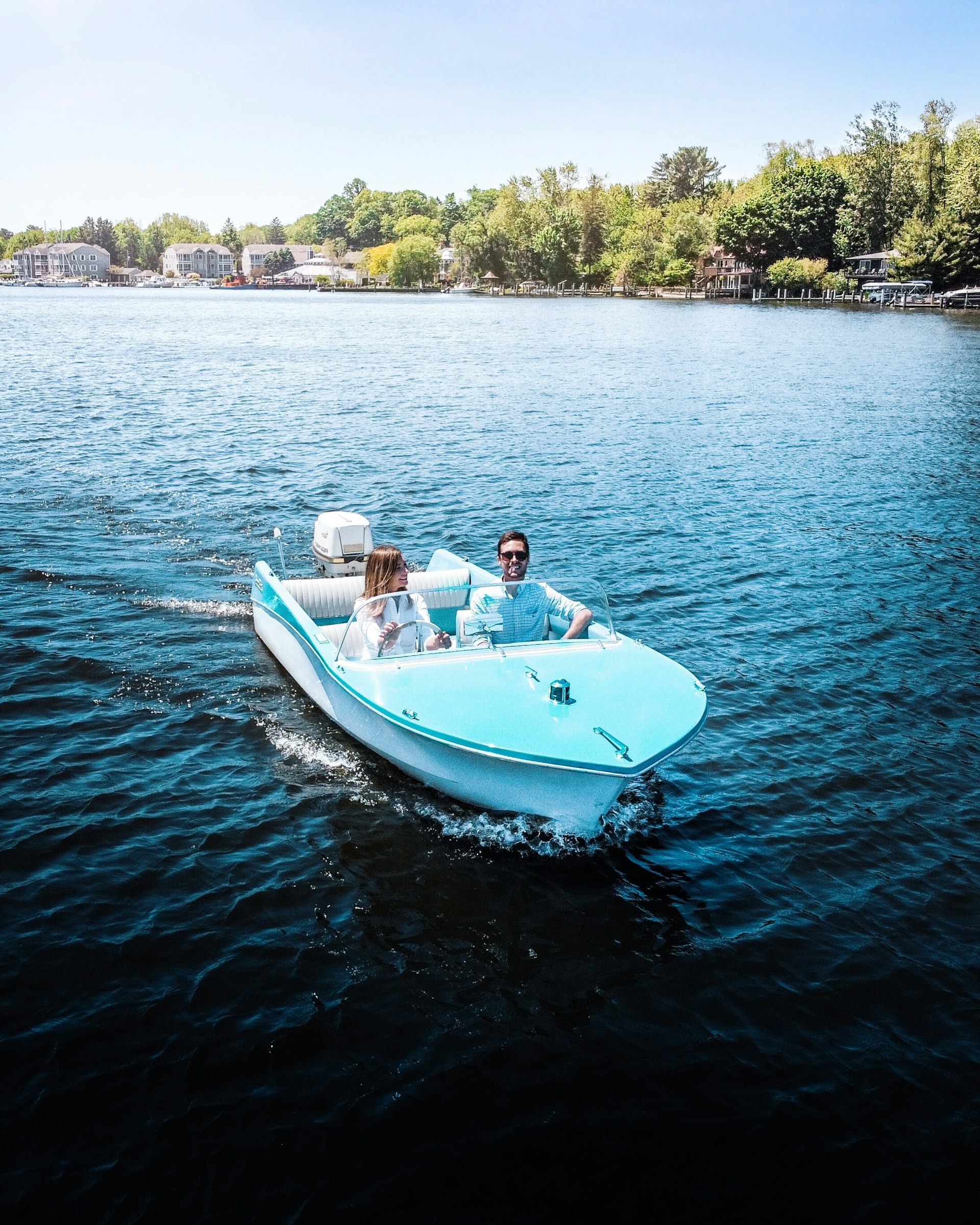 Two people ride in a light blue boat in an open body of water