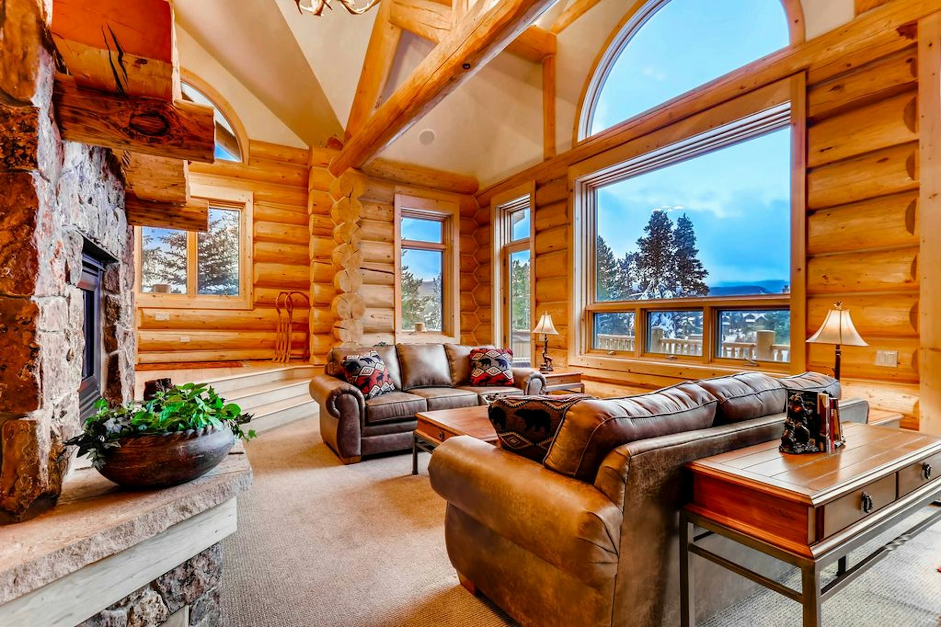 The living space at Clifton Lodge, with log walls, a stone fireplace, leather sofas, and big windows with mountain views