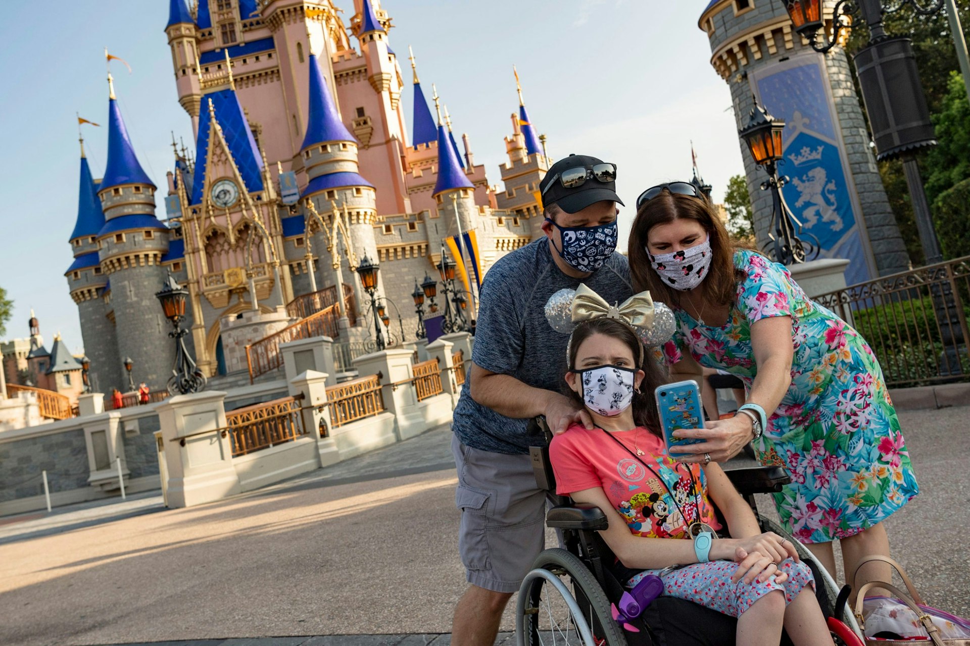 A family wearing masks with a child in a wheelchair in front of the Magic Kingdom