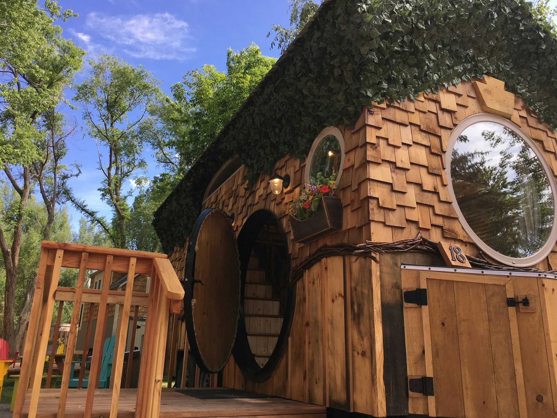 The exterior of a wooden cabin with round windows and round doorway, leading to wooden steps