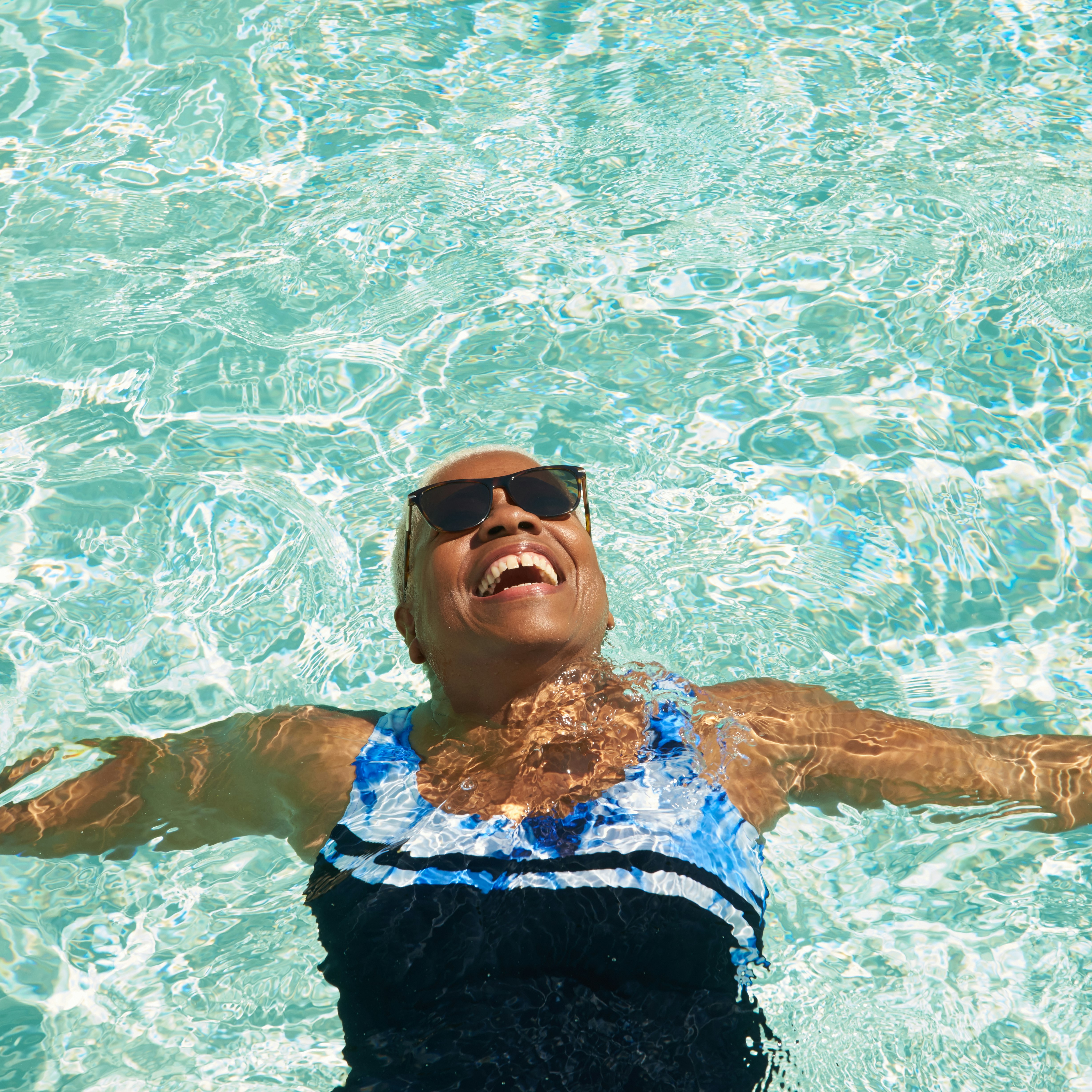 An older woman relaxes on her back in the pool enjoying the sunshine