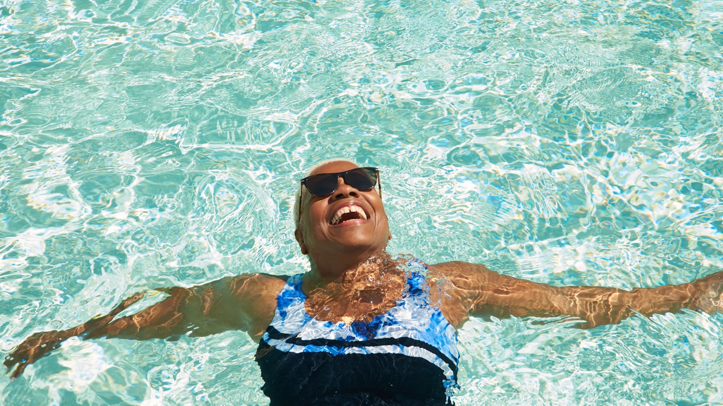 An older woman relaxes on her back in the pool enjoying the sunshine