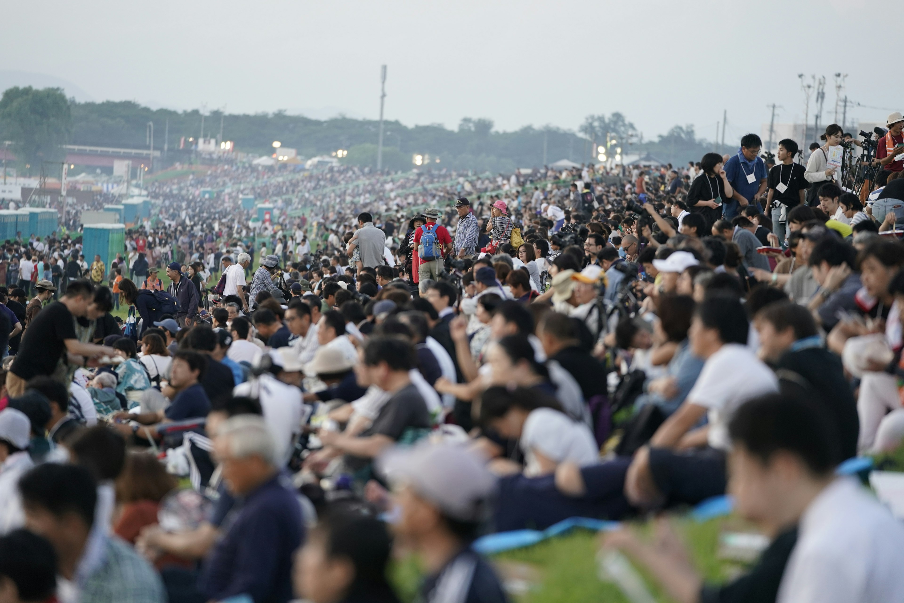 Crowds of people sit on a slope waiting for the fireworks displays