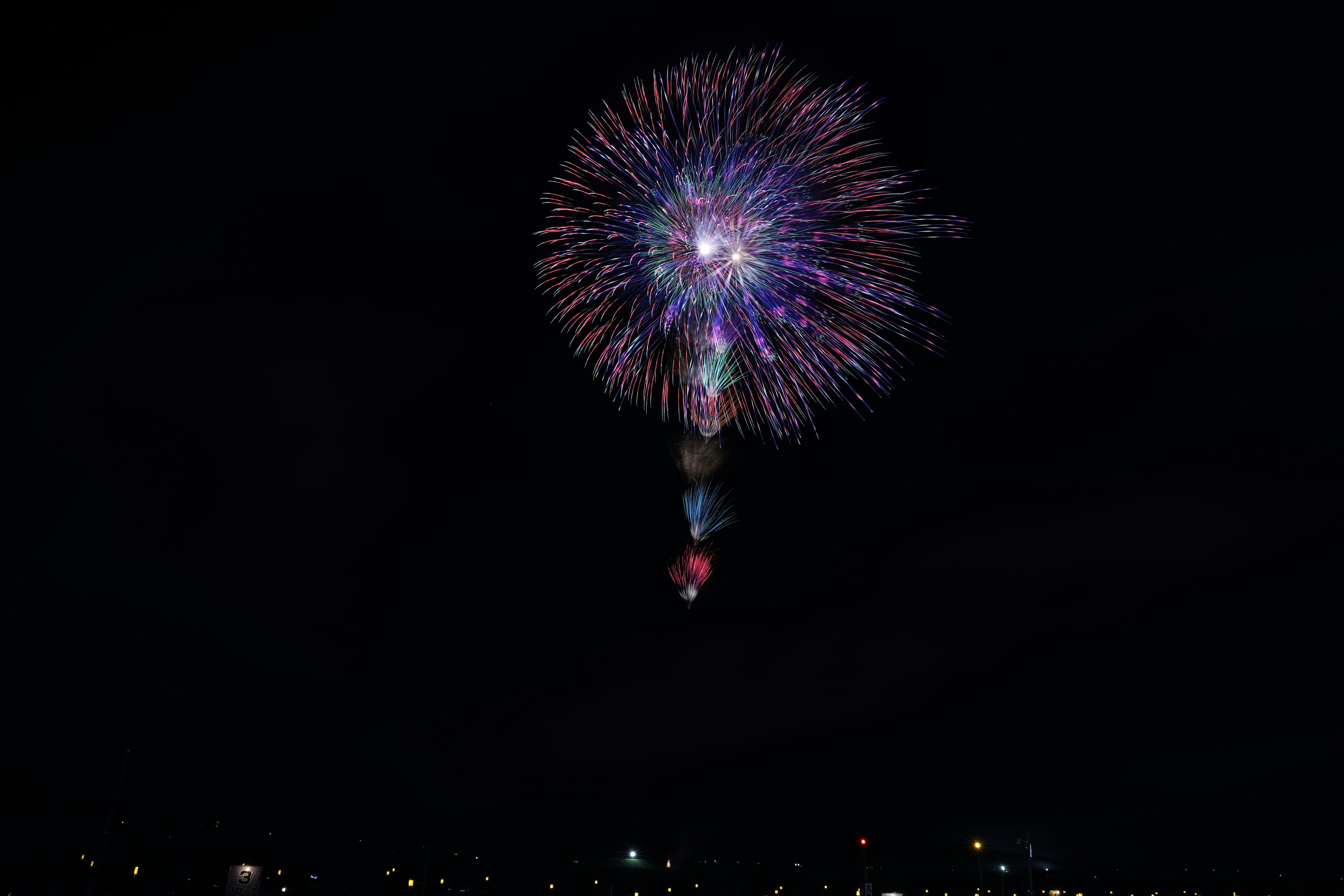 A circular firework explodes with many different colors. Below it are several other fireworks opening up into a fountain shape