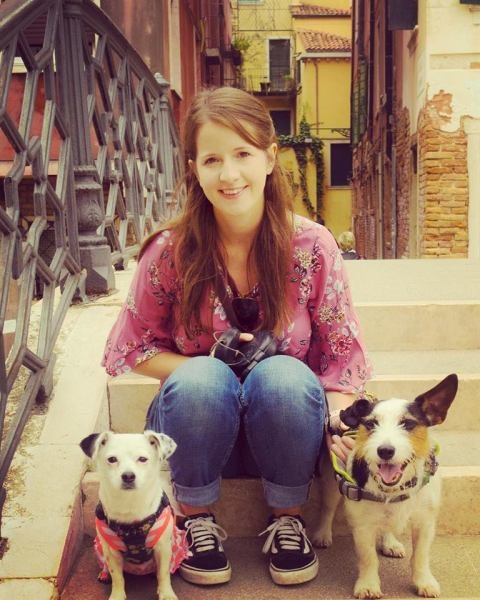 A smiling woman sits on steps with two dogs beside her
