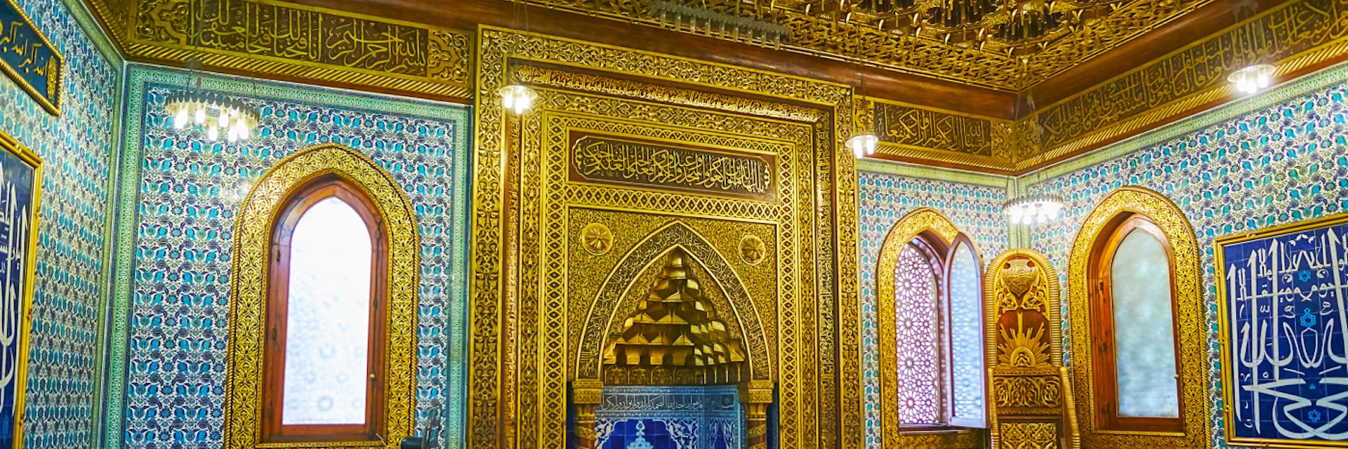 Cairo, Egypt - December 24, 2017:  Mihrab of Manial Palace mosque decorated with intricate golden patterns on carved wood, muqarnas in arch, bright blue tiles inside of niche, on December 24 in Cairo