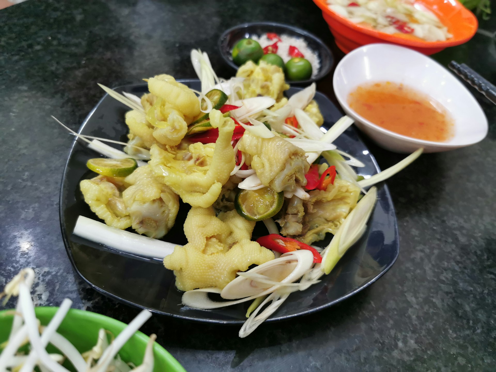 Chicken feet in a dish of lemongrass with a bowl of chilli sauce next to it