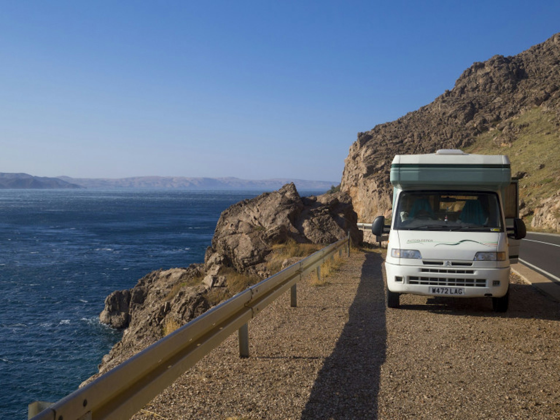 A campervan is stopped on the side of a coastal road