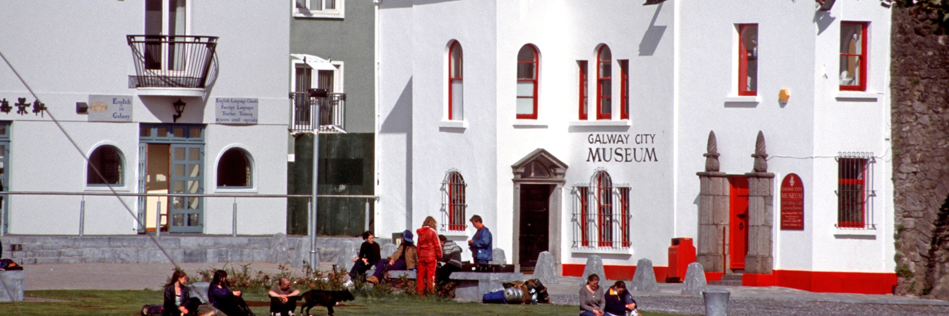 Galway, Ireland - June 17th 2005: Teenagers, some with backpacks, sitting on the bank of river Corrib, front the Galway City Museum.