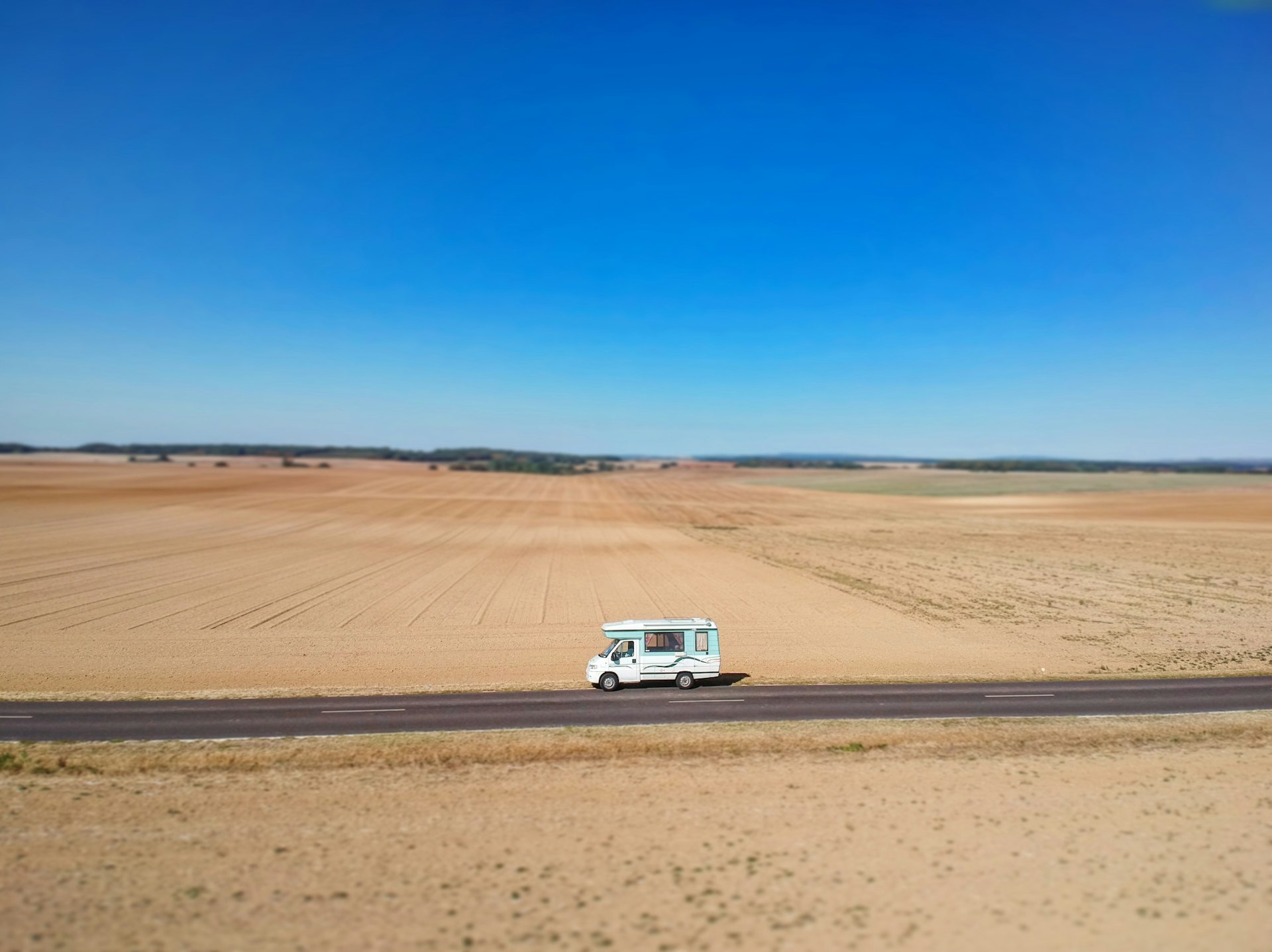An aerial view of a campervan driving through a dry landscape