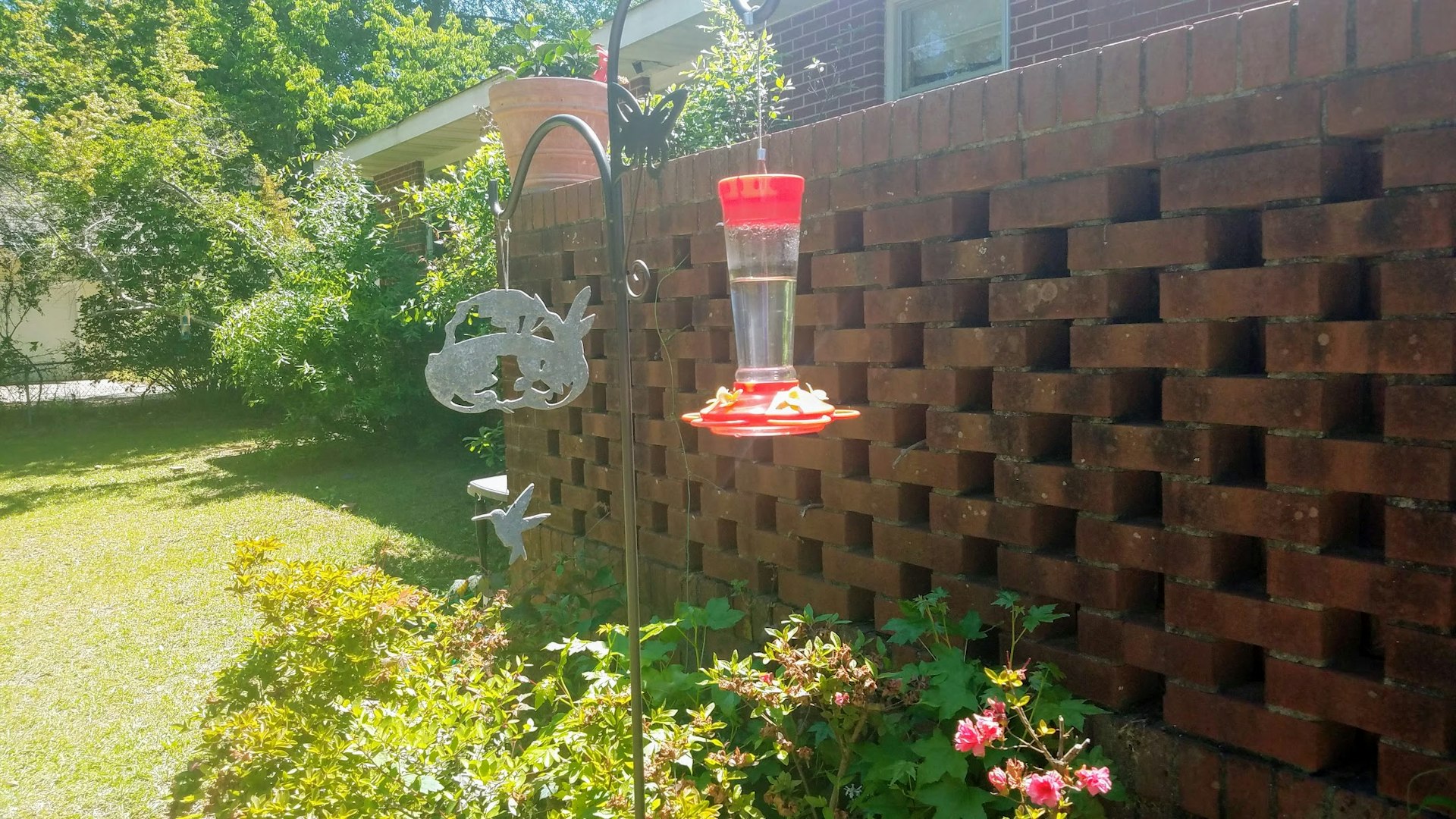 A humming bird feed hangs from a metal stand near an ornamental brick wall in Milledgeville, Georgia