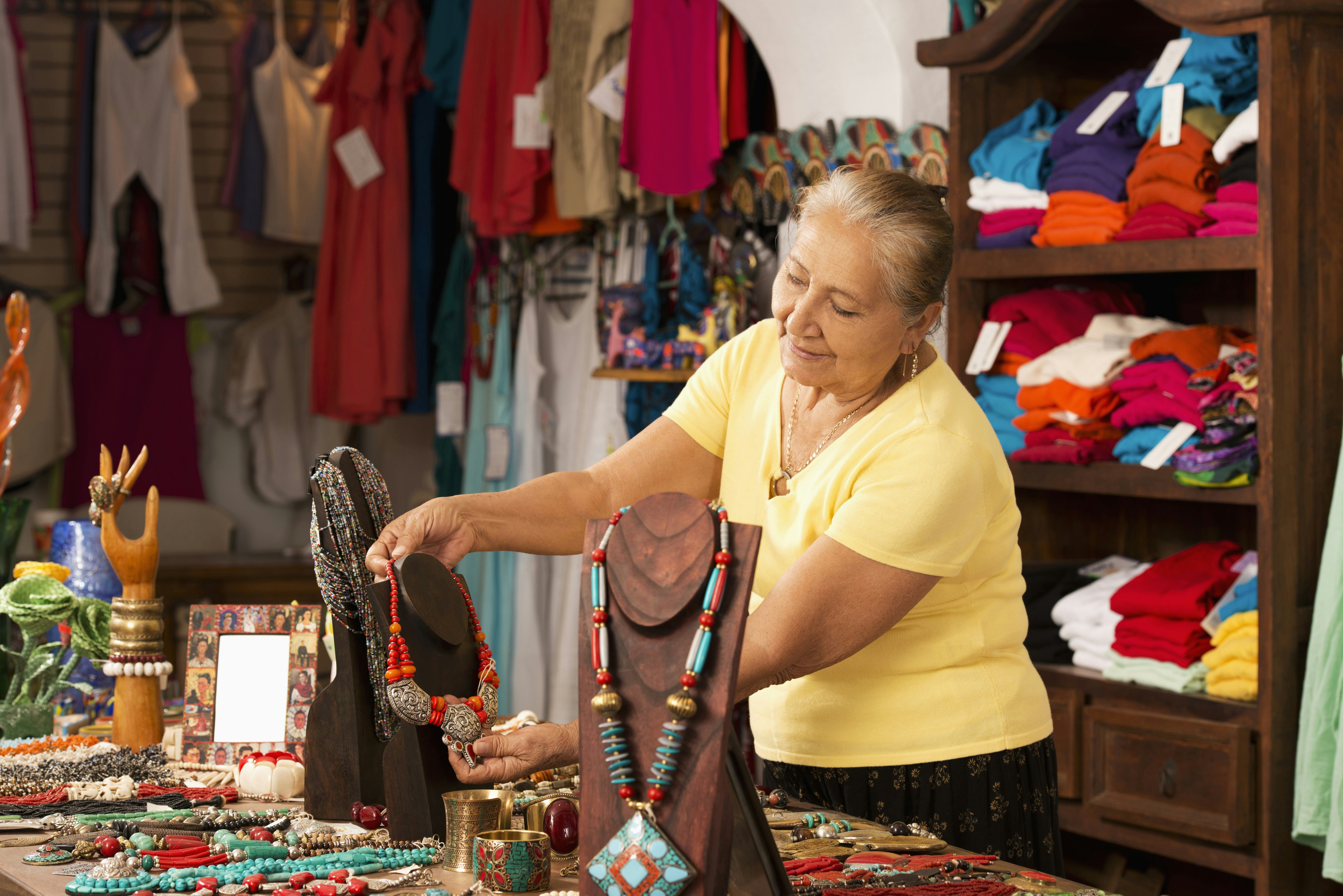 A woman arranges colourful jewellery on a display stand in a gift shop