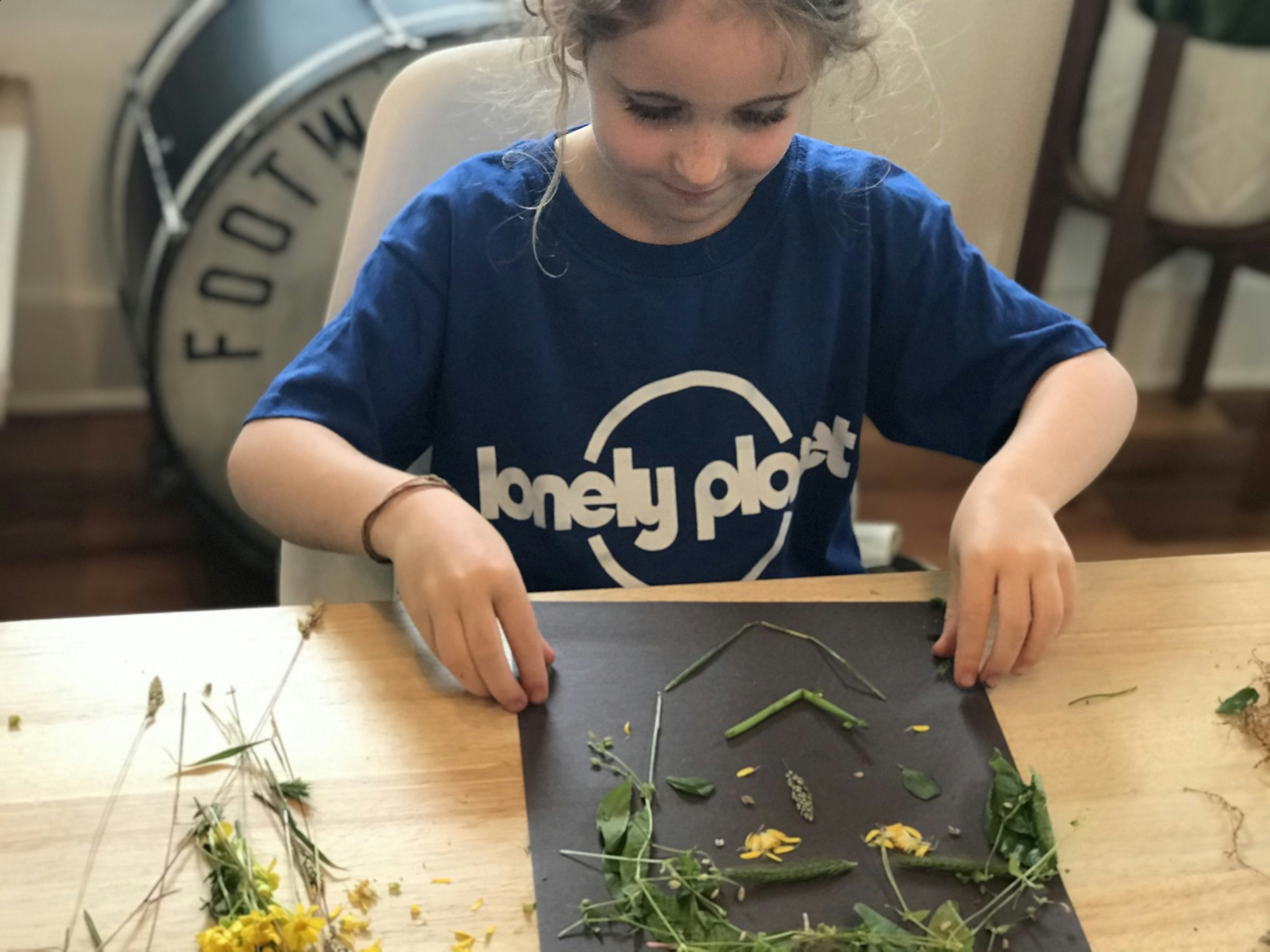 Girl uses grasses and flowers to make a face on a piece of black paper