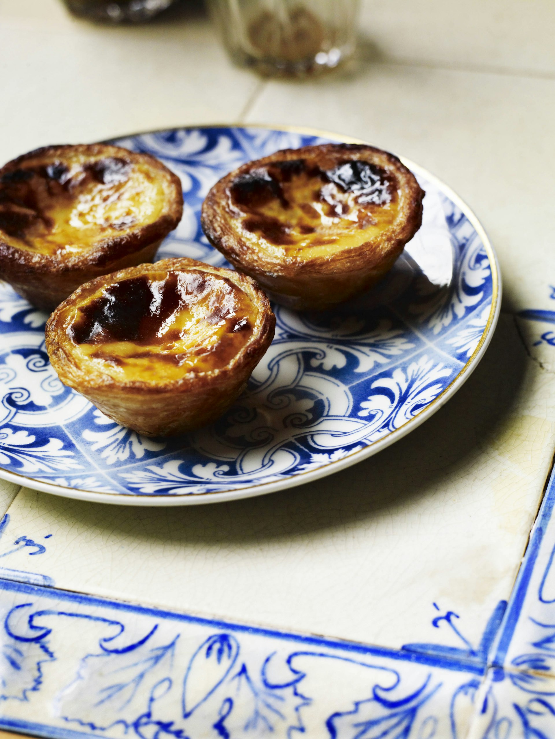 portuguese custard tarts piled on a blue and white plate