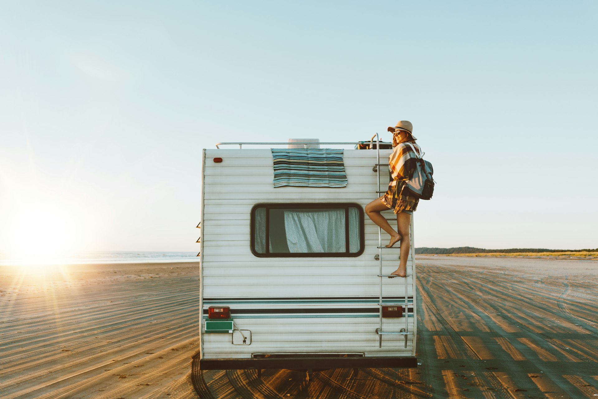 Young woman on the back of an RV, which is parked on the beach during sunset