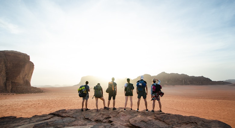 A group stands on the top of a rocky outcrop during sunset in Wadi Rum National Park.