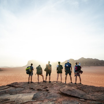 A group stands on the top of a rocky outcrop during sunset in Wadi Rum National Park.