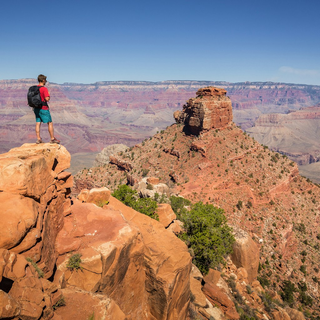 A young male hiker taking in the Grand Canyon views while standing on the edge of a rocky outcrop.