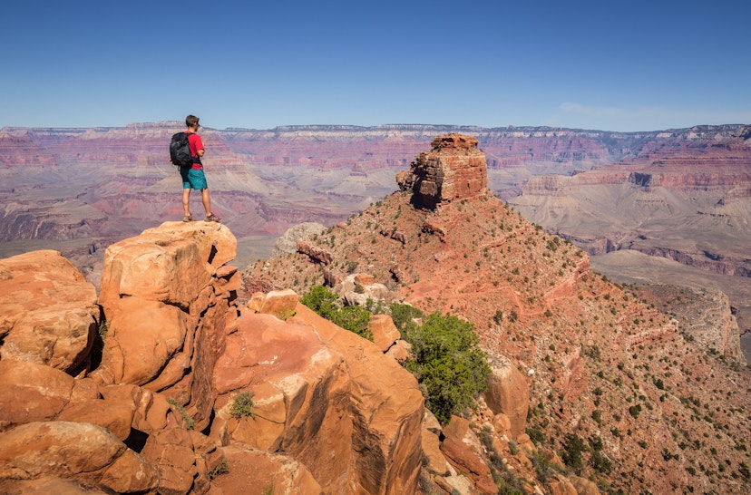 A young male hiker taking in the Grand Canyon views while standing on the edge of a rocky outcrop.
