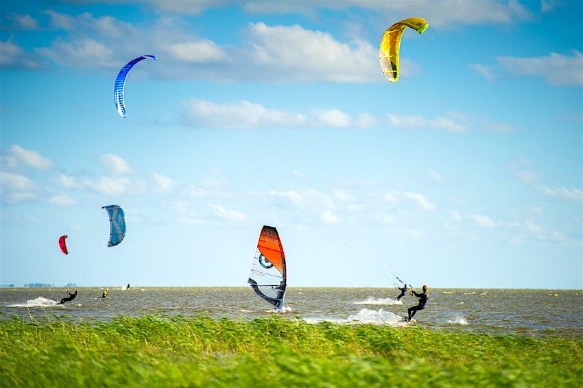 Several kitesurfers and a single windsurfer out in a lagoon