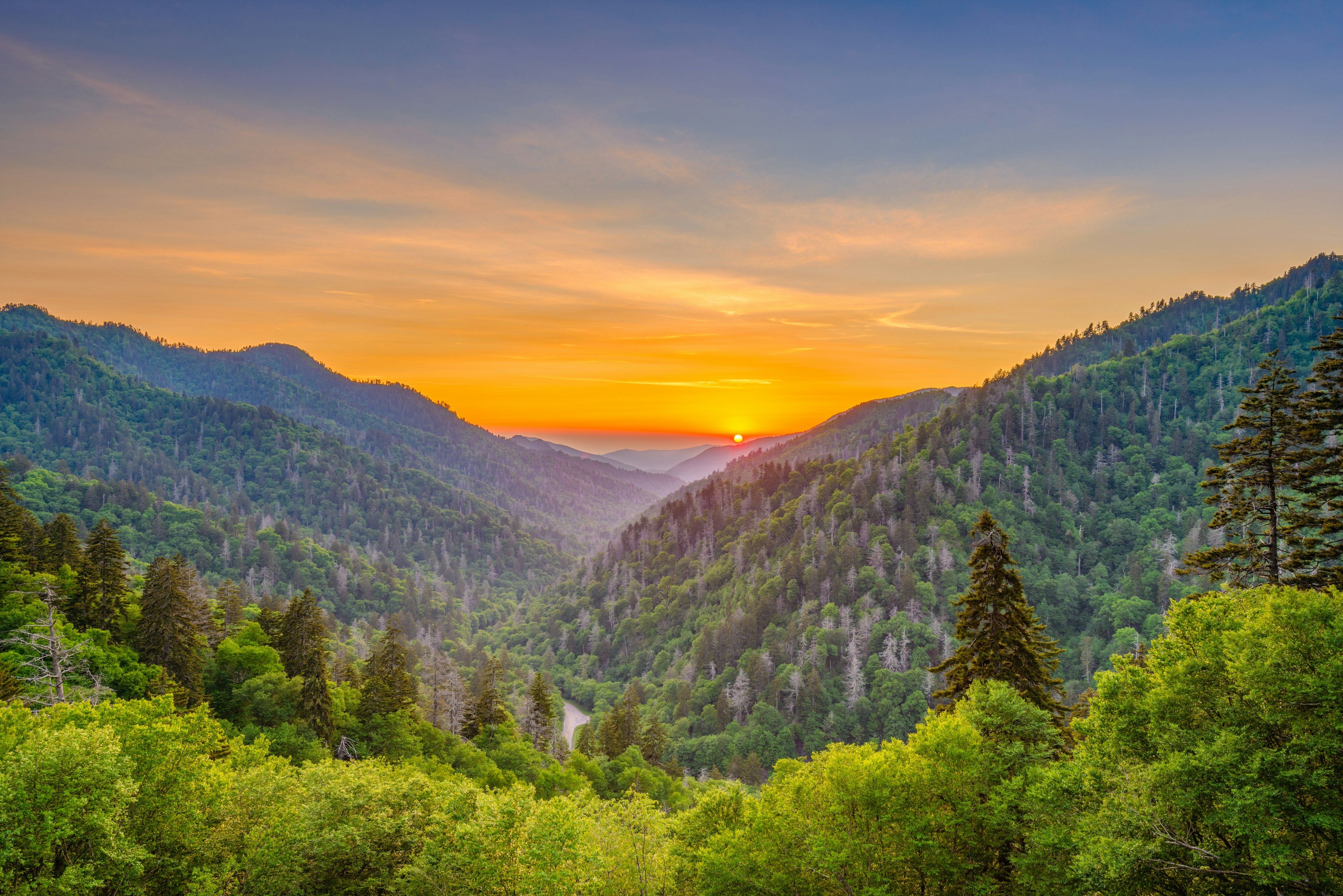 The sun sets in a valley between two mountain peaks