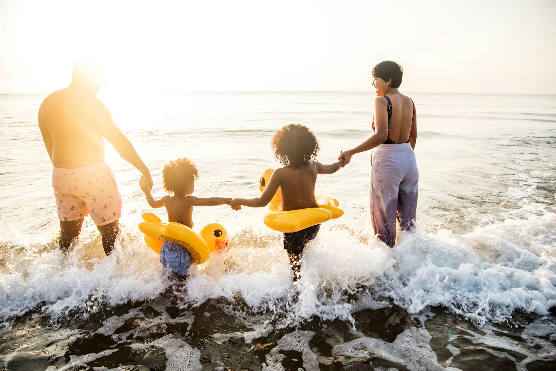 Parents with two children walking into the water at the beach while the sun sets. 