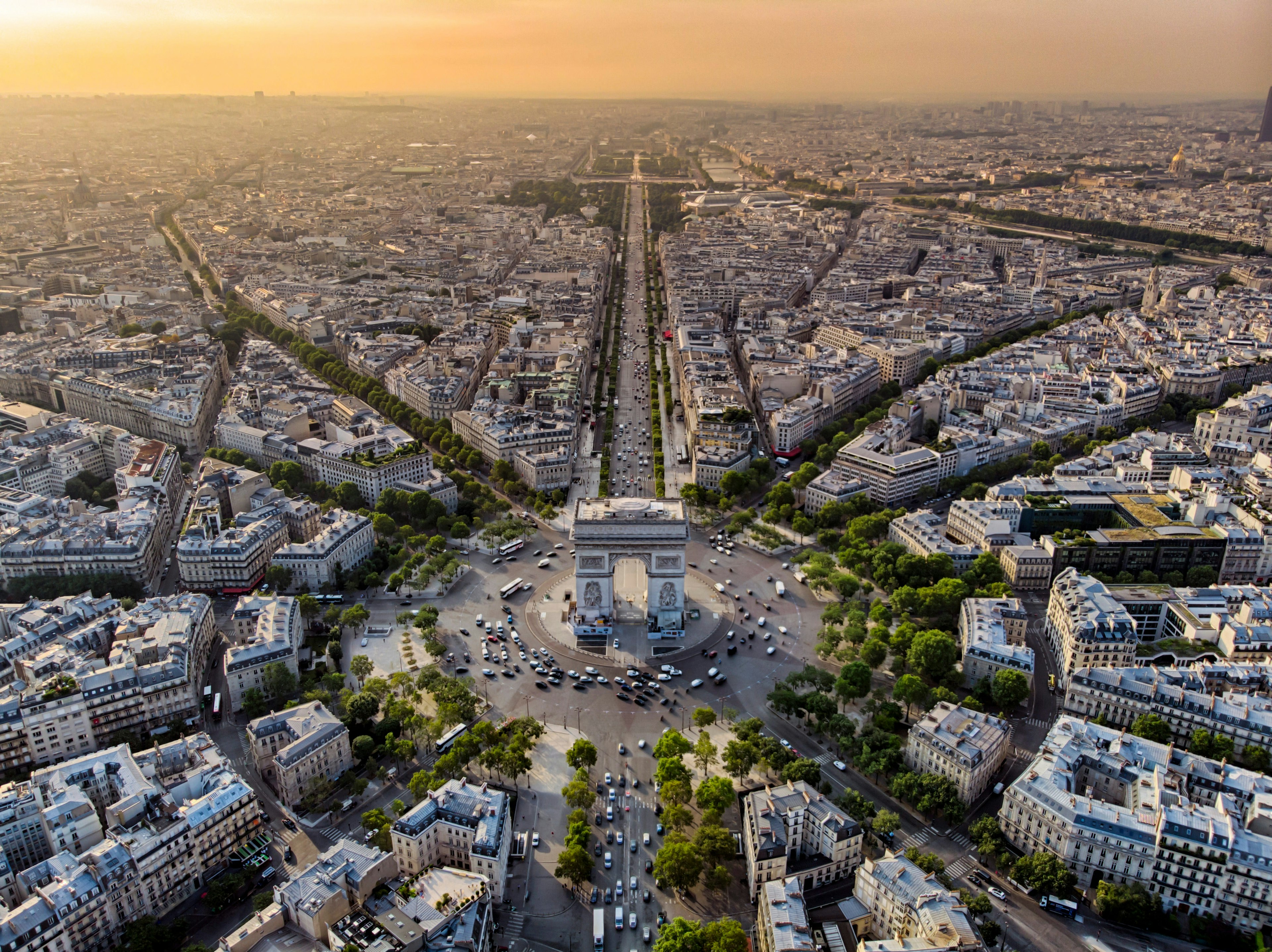 An aerial view of the Arc de Triomphe in the evening sunset with many cars on the roads that fan out from this massive landmark