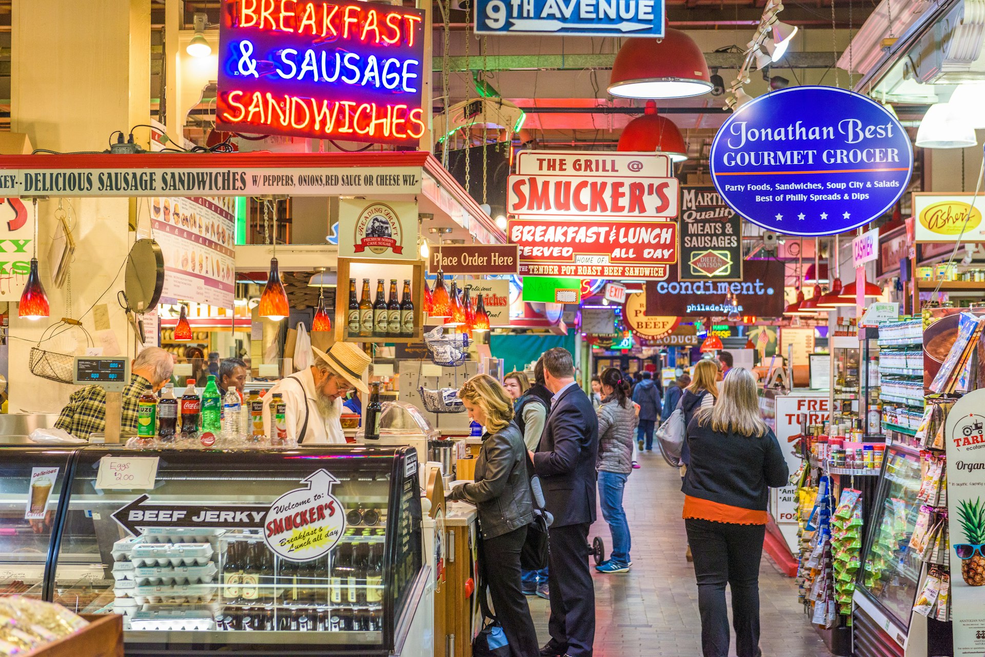 Customers shopping at Reading Terminal Market. There are large signs hanging from the ceiling. 