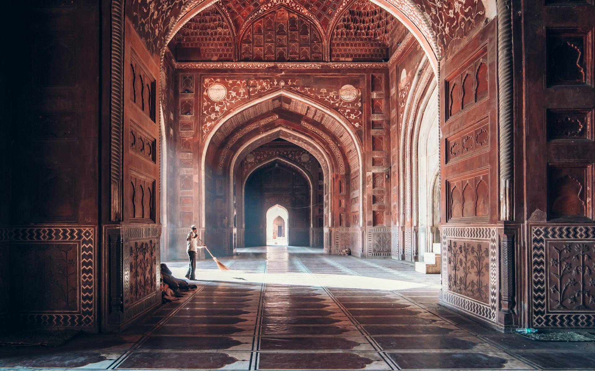 A man sweeps the floor inside the Taj Mahal mausoleum, the light streaming in behind him.