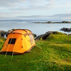 Orange camping tent on a shore in a morning light