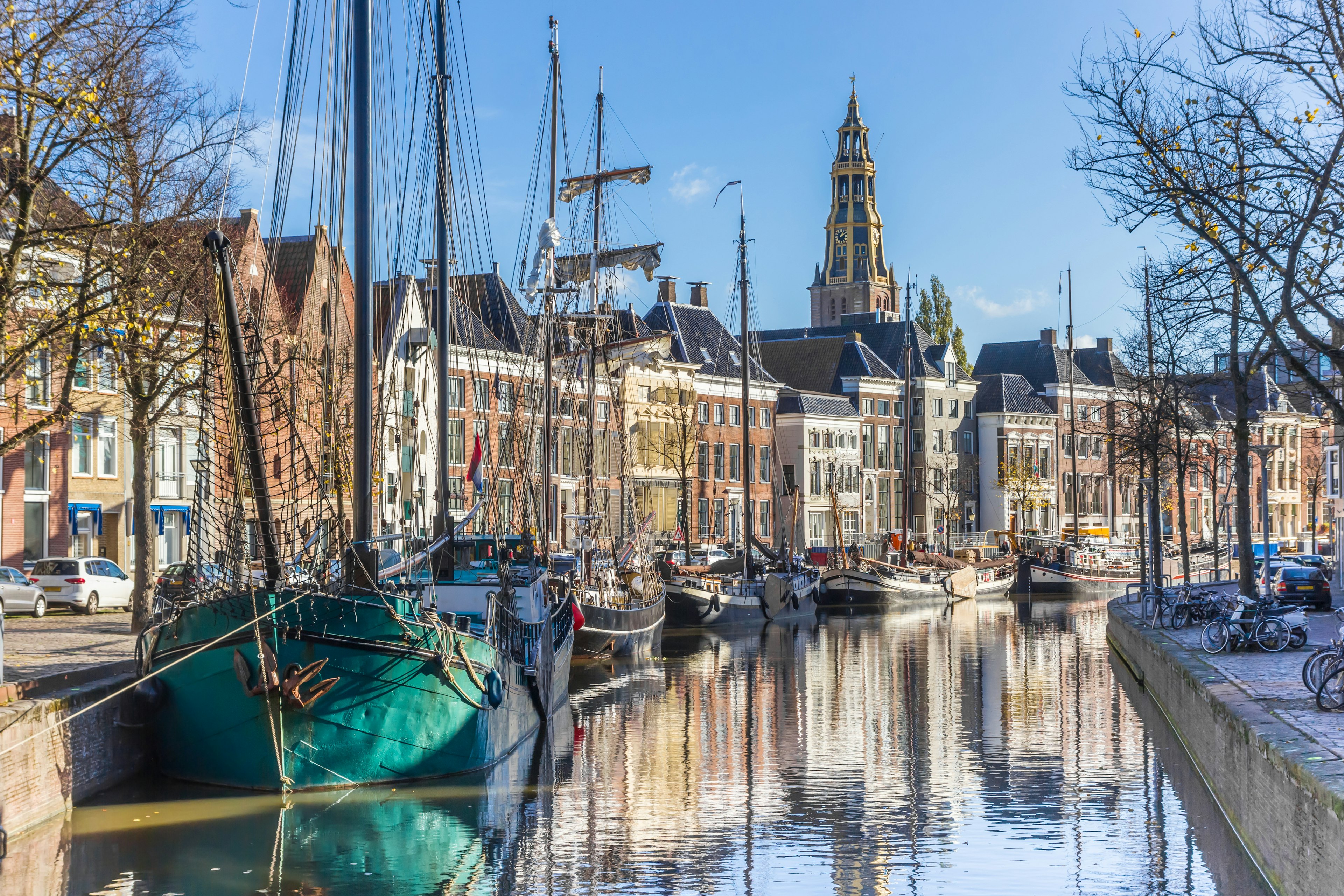 A canal lined with houses in pastel colors. Boats are docked along the left side; bikes are parked on the embankment to the right