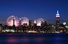 New York City skyline (with the Empire State Building) at night with fireworks in the sky on the Fourth of July.