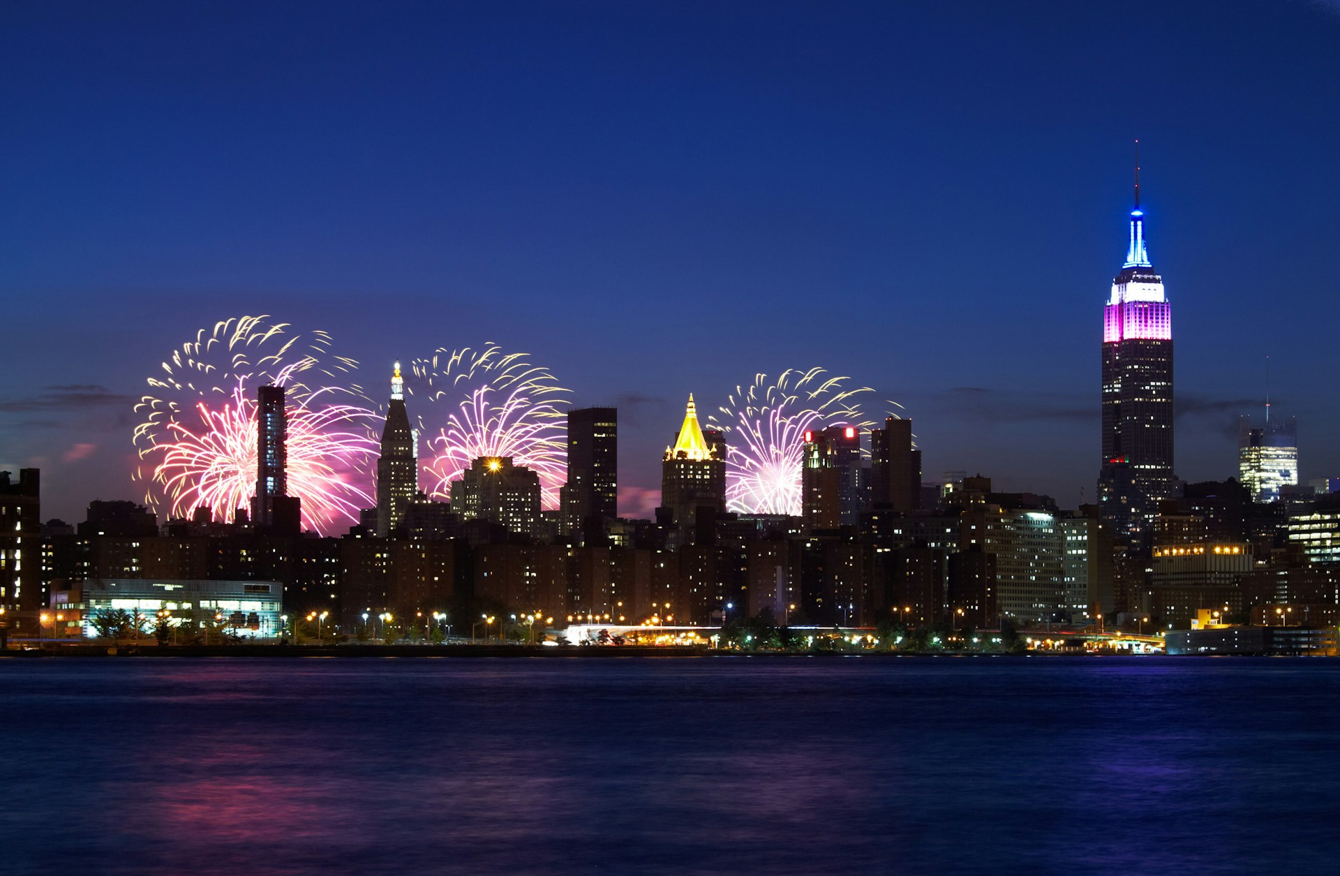 New York City skyline (with the Empire State Building) at night with fireworks in the sky on the Fourth of July.