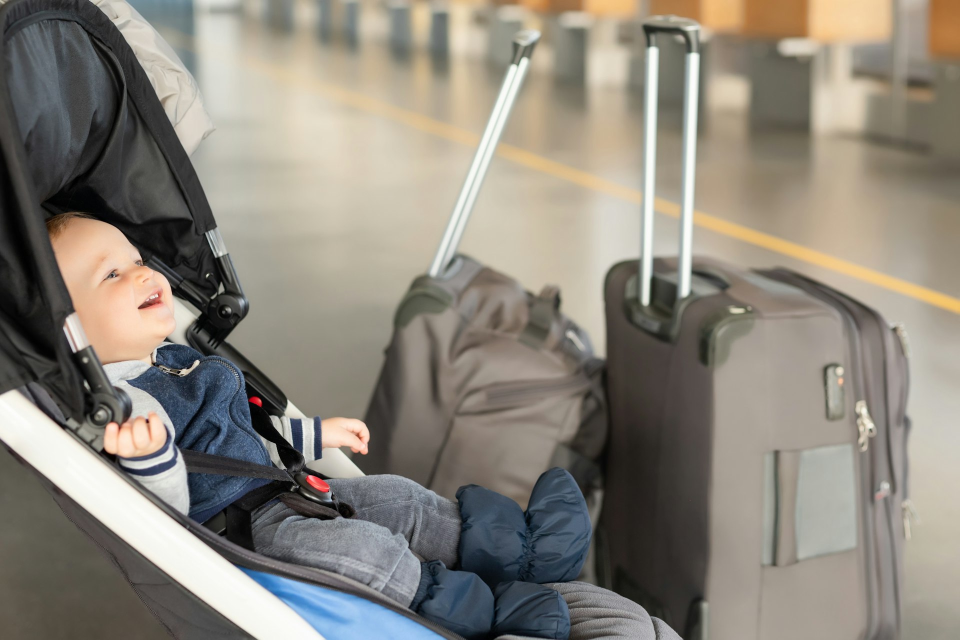 Smiling baby boy sitting in a stroller near luggage at an airport terminal