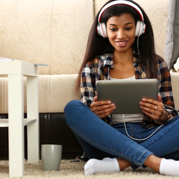 Black ordinary female american teen portrait at home sofa remote education concept. Girl hold tablet in hand music apps teacher checks homework online university library learning foreign languages