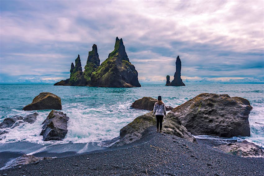 A girl approaches the rocky shore and basalt sea stacks at Reynisfjara beach.