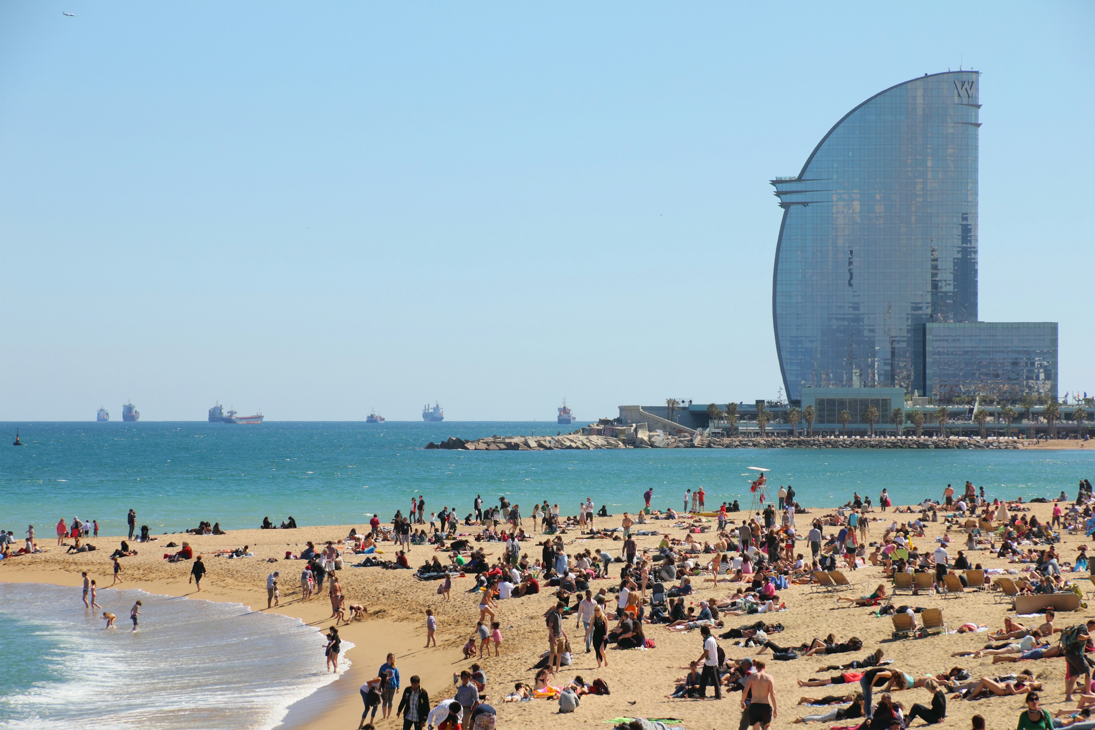 The yellow sands of Barceloneta Beach in Barcelona with the sail-shaped W Hotel in the background