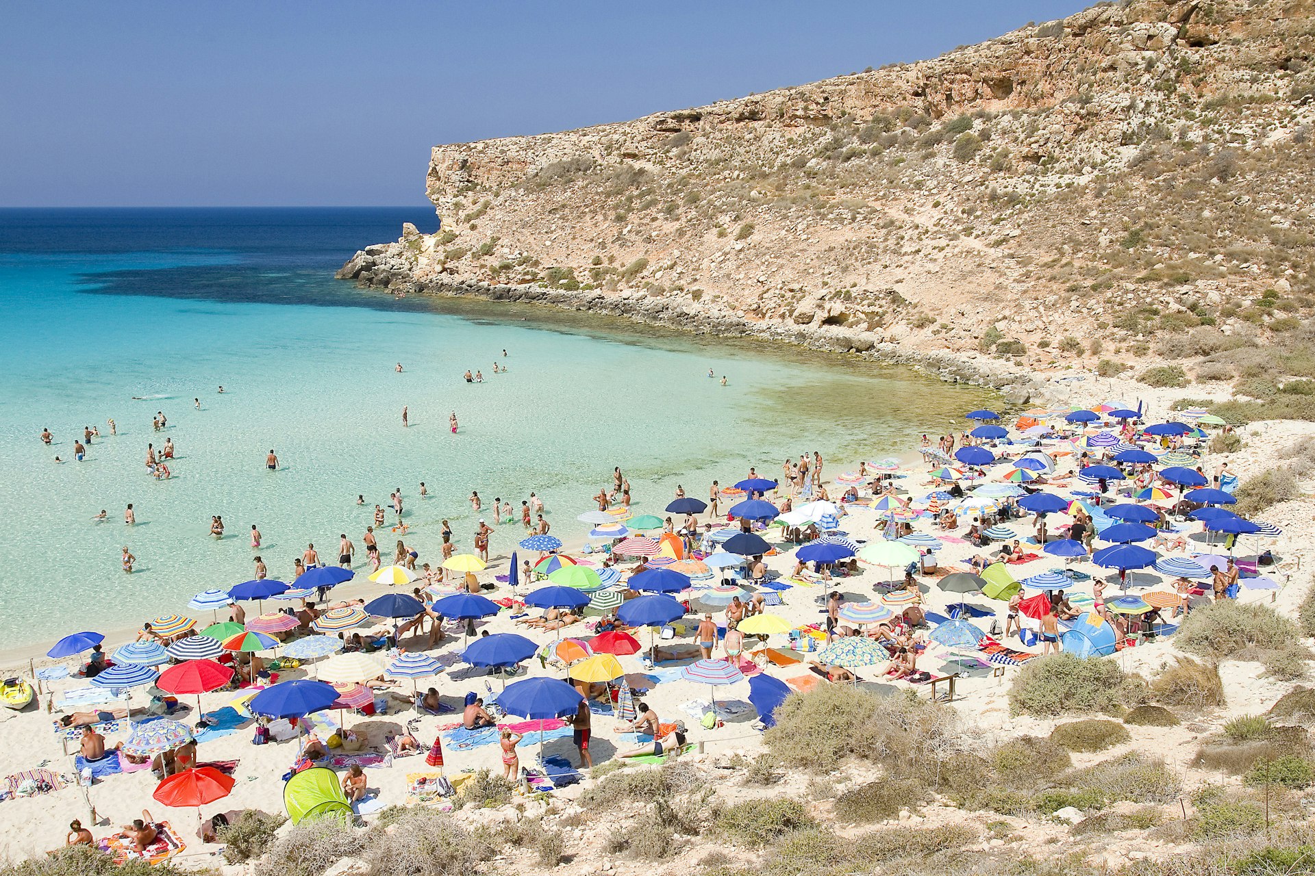 Colorful beach umbrellas cover the sand; the water is a clear and pale turquoise