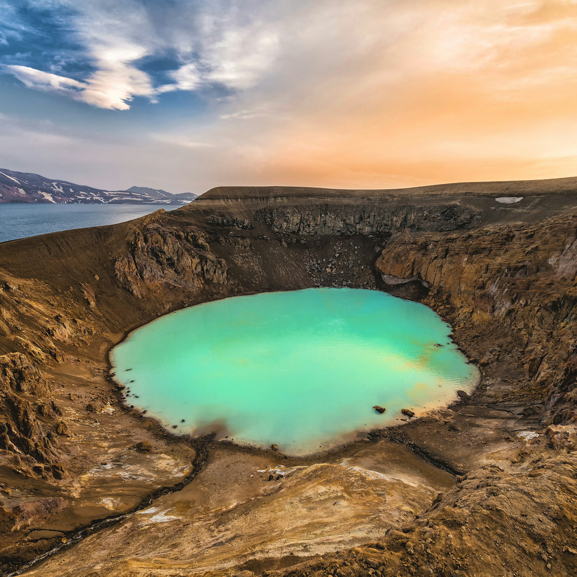A crater filled with milky blue water with a clear blue lake in the background.