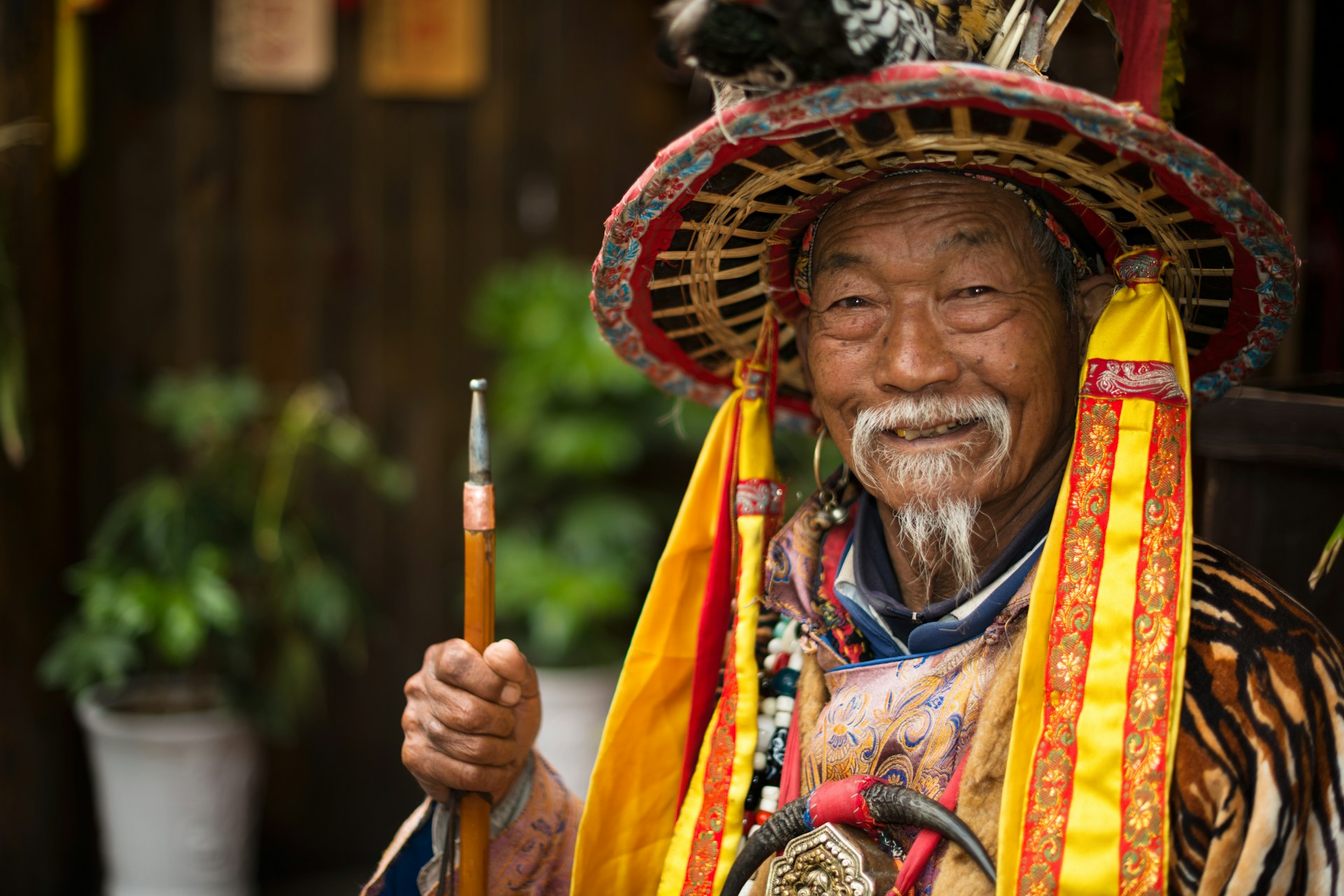 A Naxi nationality old man dressed in ancient Dongba clothing, smiling and welcome the travelers