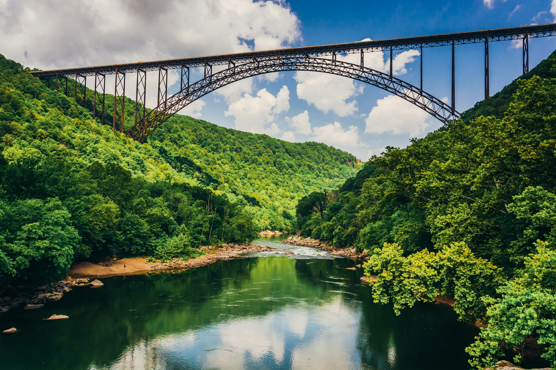The New River Gorge Bridge, as seen from Fayette Station Road on a partly cloudy day, with lush greenery on either shore